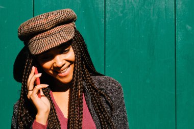 Örgülü siyah kadın akıllı telefonuyla telefon görüşmesi yapıyor.