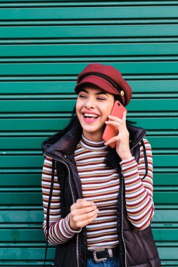 Ortadoğulu genç bir kız açık havada kırmızı bir akıllı telefon kullanıyor.