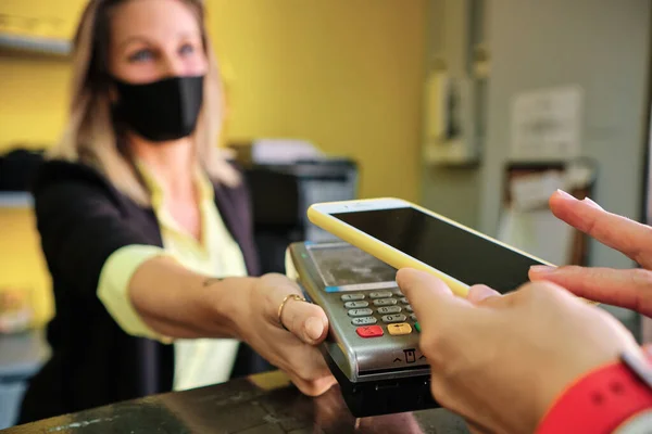 woman with protective mask using credit card to pay contactless - new normal