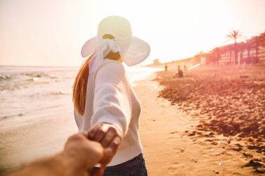 Plajda şapkası olan tanınmamış genç bir kadın turistik bir yerde erkek arkadaşına yardım ediyor.