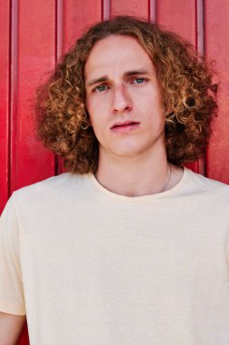Kıvırcık saçlı, yeşil gözlü şık bir genç adam kameraya bakıyor.