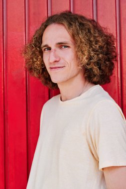 Kıvırcık saçlı, yeşil gözlü, gülümseyen ve kameraya bakan şık bir genç.