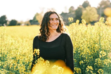 İlkbaharda kolza tohumu tarlasında genç, tatlı kavisli bir kadın.