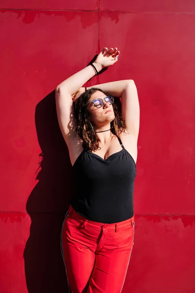 Jovem mulher curvilínea com óculos com um fundo vermelho olhando para o sol — Fotografia de Stock