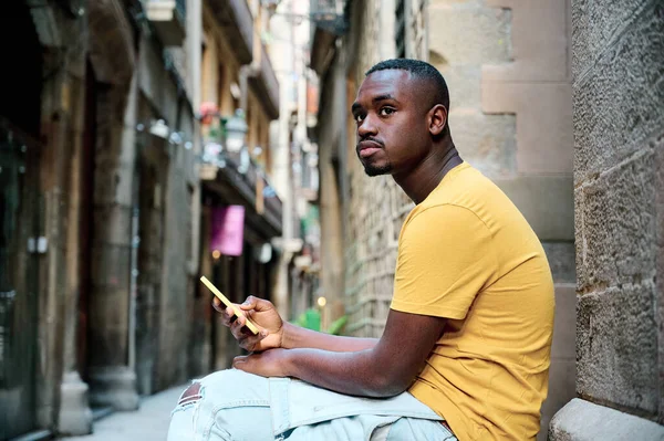 바르셀로나의 오래 된 도시에 앉아 스마트폰을 사용하는 젊은 흑인 여성 — 스톡 사진