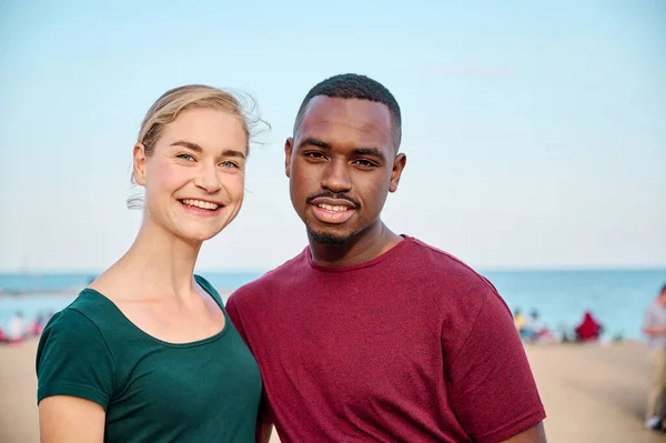 Joven pareja multiétnica mirando a la cámara en la playa — Foto de Stock