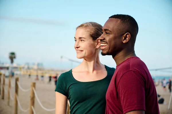 Joven pareja multiétnica en la playa mirando fuera de la cámara con espacio de copia y sonriendo — Foto de Stock