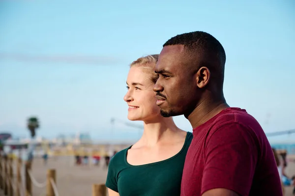 Joven pareja multiétnica en la playa mirando fuera de la cámara con espacio de copia — Foto de Stock