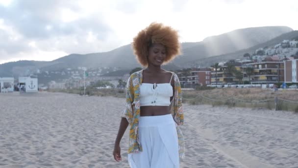 Joven mujer negra sonriendo y caminando sobre la arena — Vídeos de Stock