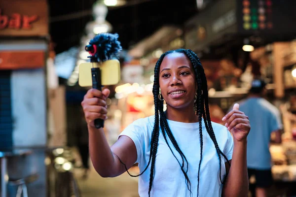 Jovem influenciador latino-americano africano usando smartphone e microfone para transmissão ao vivo — Fotografia de Stock