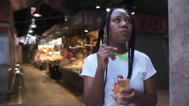 Junge afrikanisch-amerikanische Frau isst gesunde Früchte auf einem lokalen Markt — Stockvideo