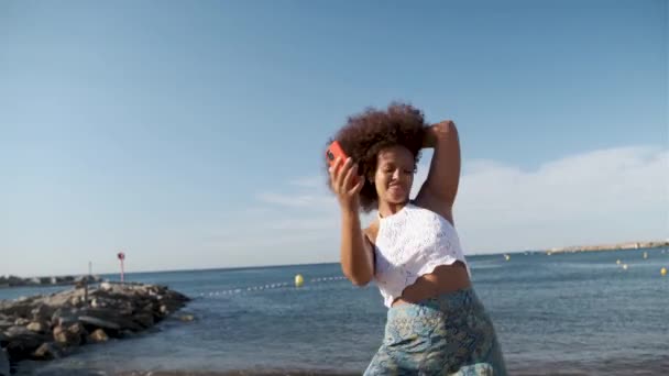 Πραγματική καμπυλωτή γυναίκα που χορεύει με smartphone στην παραλία — Αρχείο Βίντεο