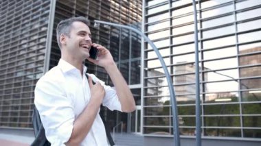 Modern şehirde gülümseyen ve akıllı telefon kullanan genç bir adam.