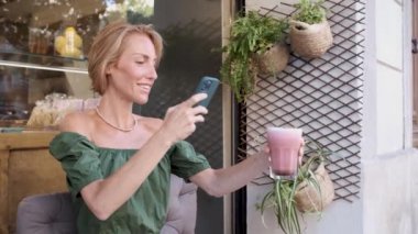 Viral video için akıllı telefon ve smoothie kullanan yetişkin zinde bir kadın. Etkileyici konsept.