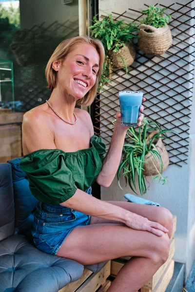 Hubená zdravá žena dívající se do kamery a ukazující smoothie — Stock fotografie