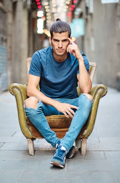 Genç ve yakışıklı bir adam kameraya bakıyor ve Barselona El Borne Bölgesi 'ndeki koltukta oturuyor.