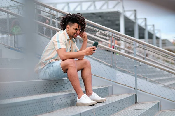 Giovane uomo latinx utilizzando smartphone e sorridente mentre cerca video virali — Foto Stock