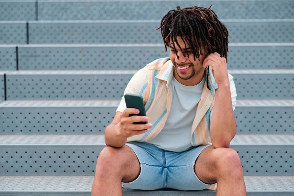 Joven latinx hombre sonriendo mientras busca teléfono inteligente —  Fotos de Stock