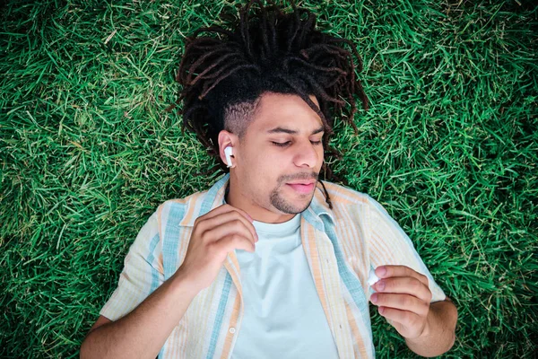 Joven escuchando música con auriculares y acostado en la hierba —  Fotos de Stock