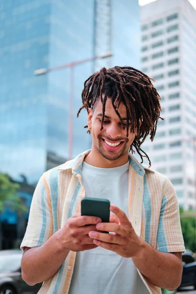 Foto vertical de un joven latino con pelo rizado en la ciudad usando smartphone —  Fotos de Stock