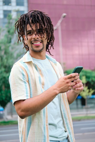 Retrato vertical del hombre latino con el pelo rizado mirando a la cámara y con un smartphone —  Fotos de Stock