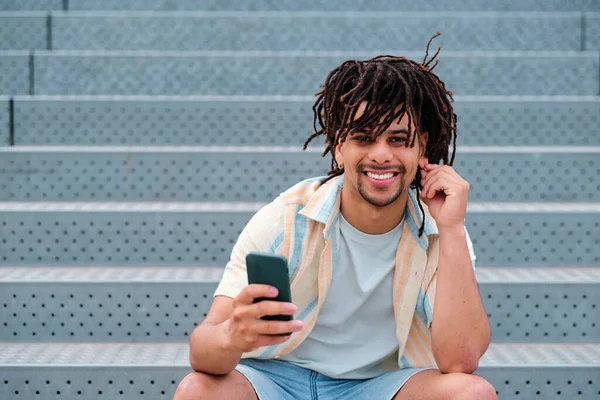 Primo piano di giovane uomo latino con i capelli ricci guardando la fotocamera e tenendo in mano uno smartphone — Foto Stock