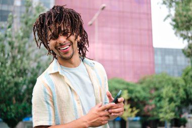 young man at the city smiling and looking at camera with smartphone clipart
