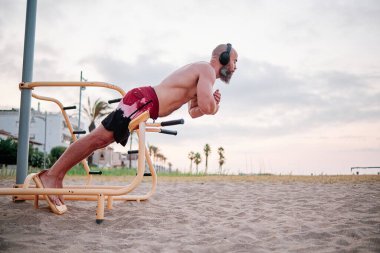 Atletik adam dışarıda jimnastik yaparken karın kaslarını çalıştırıyor..