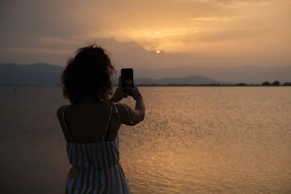 Vrouw met behulp van haar mobiele telefoon om foto 's te nemen naar de zonsondergang. — Stockfoto