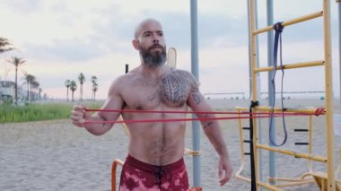 Fitness adamı plajda dirençli lastik bant ile beden eğitimi yapıyor. Spor konsepti.