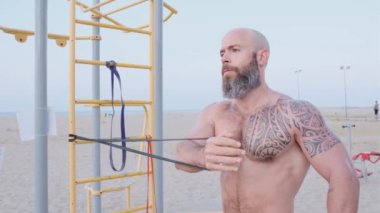 Spor salonundaki adam plajda dirençli lastik bant ile göğüs egzersizi yapıyor. Spor konsepti.