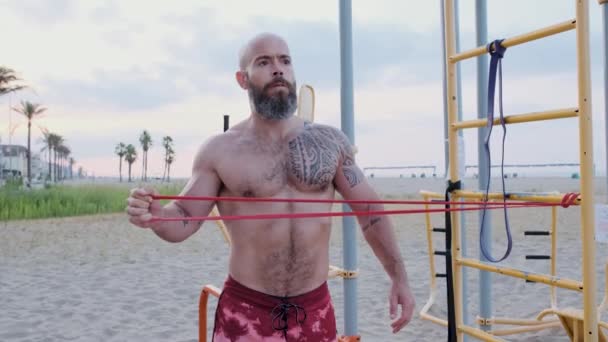 Homem de fitness fazendo exercícios de calistenia com um elástico de resistência na praia. Conceito de desporto. — Vídeo de Stock