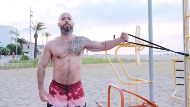 Fitness człowiek robi ćwiczenia gimnastyczne klatki piersiowej z gumką oporową na plaży. Koncepcja sportu. — Wideo stockowe