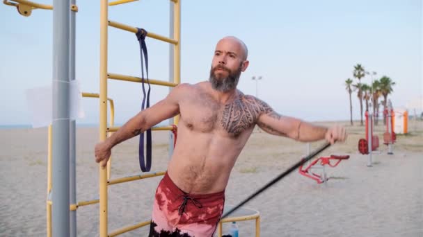 Fitness man doet weer calisthenics workout met een weerstand rubberen band op het strand. Sport concept. — Stockvideo