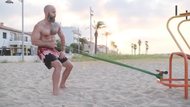 Homem de fitness fazendo exercícios de calistenia com um elástico de resistência na praia. Conceito de desporto. — Vídeo de Stock