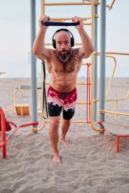 Kumsalda lastik bantla egzersiz yapan sporcu..