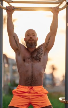 Erkek sporcu açık havada antrenman yaparken barın önünde duruyor..