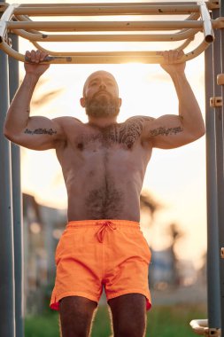 Gün batımında dışarıda idman yaparken barfiks çeken güçlü bir adam..