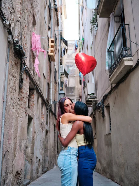 Leszbikus pár ölelkezik, miközben egy piros szív alakú lufit tart az utcán.. — Stock Fotó