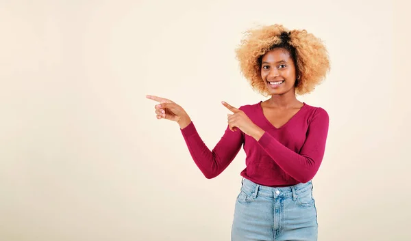 Felice afro donna che punta al lato per presentare o promuovere qualcosa mentre in piedi su uno sfondo isolato. — Foto Stock