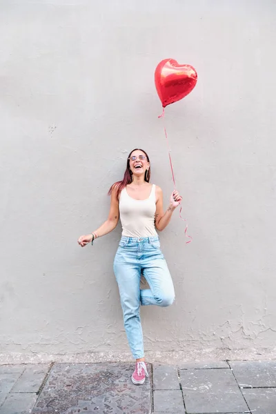 Lycklig kvinna håller en röd hjärtformad ballong utomhus på gatan. — Stockfoto