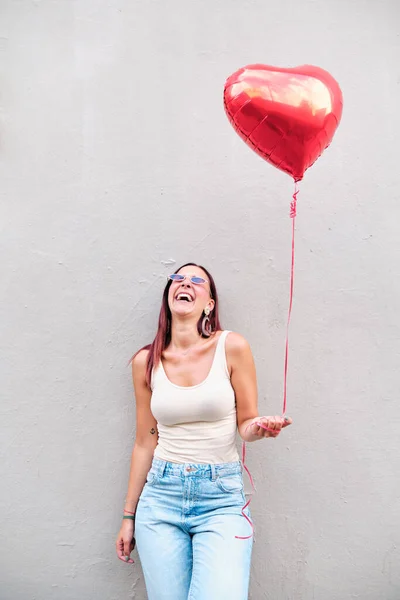 Ung kvinna skrattar medan du håller en röd hjärtformad ballong utomhus. — Stockfoto