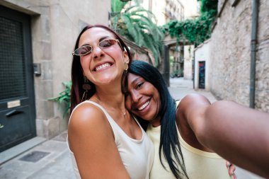 İki bayan arkadaş kasabada yürürken selfie çekiyorlar..