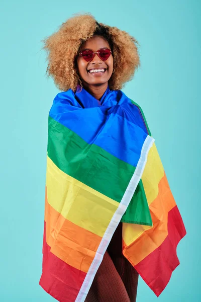 LGBTQ toplumunu desteklemek için gökkuşağı bayrağına sarılmış gülümseyen Afro kadın.. — Stok fotoğraf