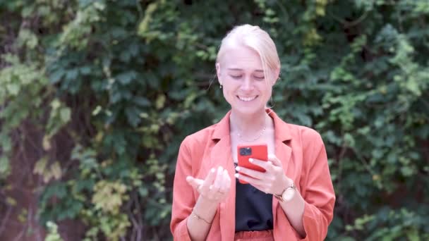 Молода жінка посміхається і прокручує екран свого смартфона — стокове відео