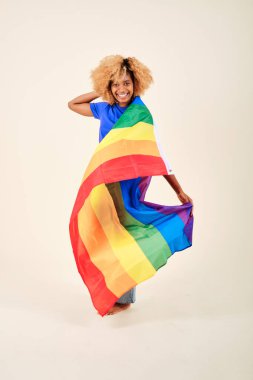 Smiling curly hair woman holding an lgbt pride rainbow flag over an isolated background. clipart