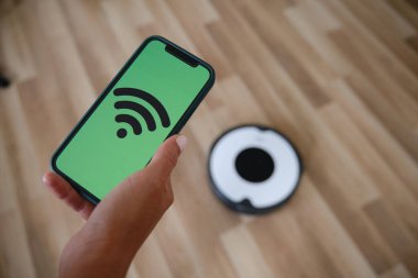 Kadın, robot elektrik süpürgesini kontrol etmek için cep telefonunda akıllı ev uygulaması kullanıyor..