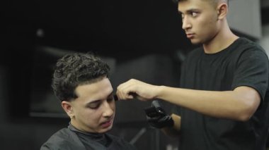 Profesyonel bir kuaförün erkek müşterinin saçını budayıcı ile keserken yakın plan görüntüsü. Berber modaya uygun bir saç kesimi yapıyor.