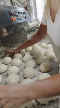 Hamur toplarını ustalıkla yoğurup şekillendiren deneyimli bir fırıncı. Fırında un kaplı bir granit tezgahta çalışan ellerin detaylı görüntüsü