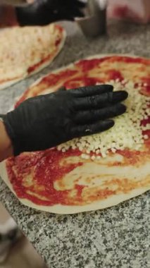 Lokanta mutfağında bir şefin çiğ pizza hamurunun üzerine küp mozzarella peyniri dökerek eldivenli ellerini kapamasını.